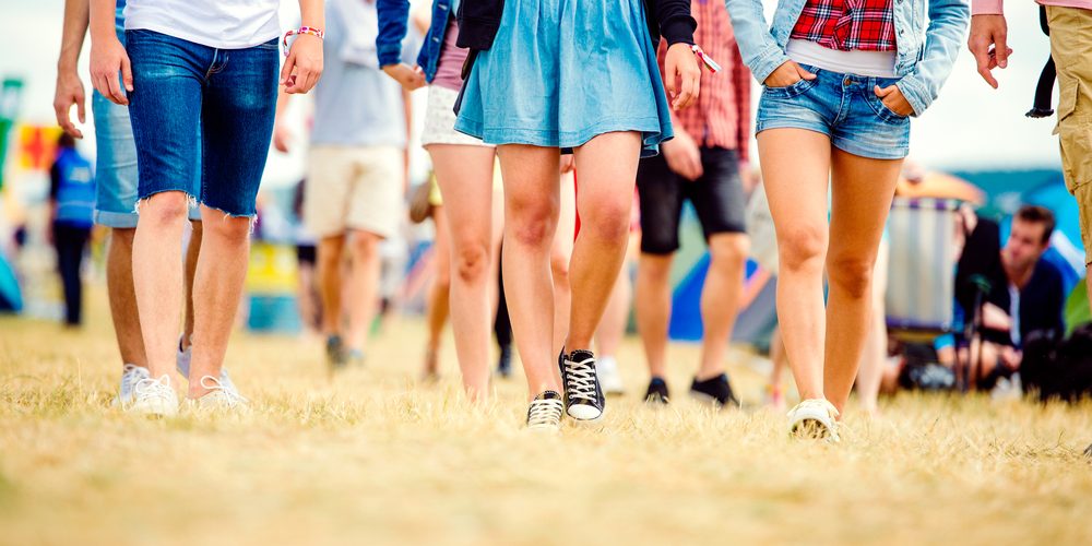 Unrecognizable teenagers at tent music festival walking, sunny summer, close up of legs